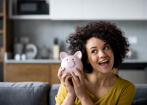 Woman excited about saving money with water softener OKC. She is holding a pink piggy bank.
