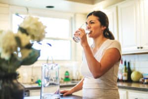 Pretty woman drinking clean water using a whole house water filter.