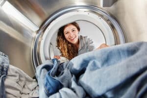 Young woman with water softener system pulling clean and soft laundry out of dryer.
