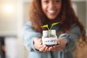 Irrigation well will save money by reducing your municipal water usage cost. Young woman holding out jar labeled savings growing small green leafed plant.