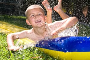 Water slide and kid. A kid slides down a slippery water slider during a hot summer day. Summer water well efficiency and well service - JB Water Well